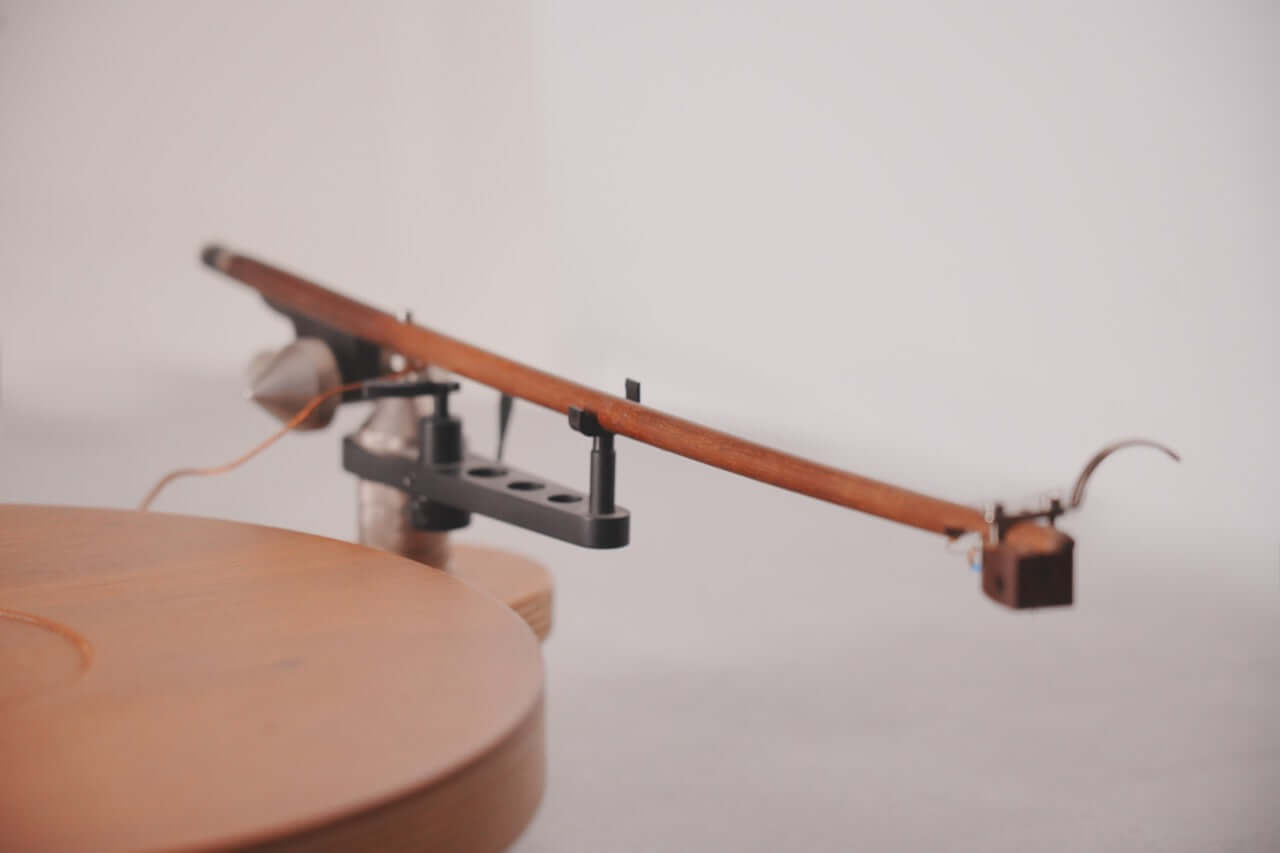 A close-up of the Arco 40 Plattenspieler shows its wooden tonearm on a vinyl turntable, emphasizing minimalist, modern design against a neutral, blurred background.