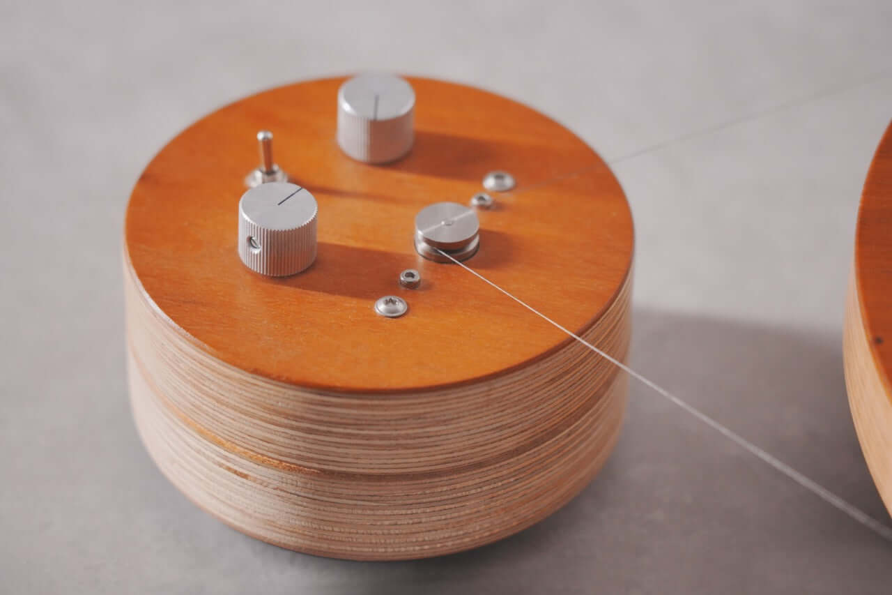 A close-up of the Arco 40 Plattenspieler, a round wood turntable with metal knobs, screws, and a thin wire extending from it, set on a light surface.