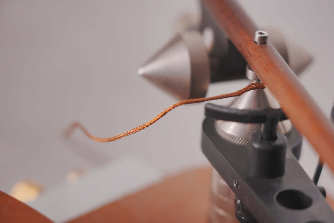 Close-up of a braided copper wire attached to a metallic part of the Arco 40 Plattenspieler, showcasing precision similar to wood turntable components, against a blurred gray background.