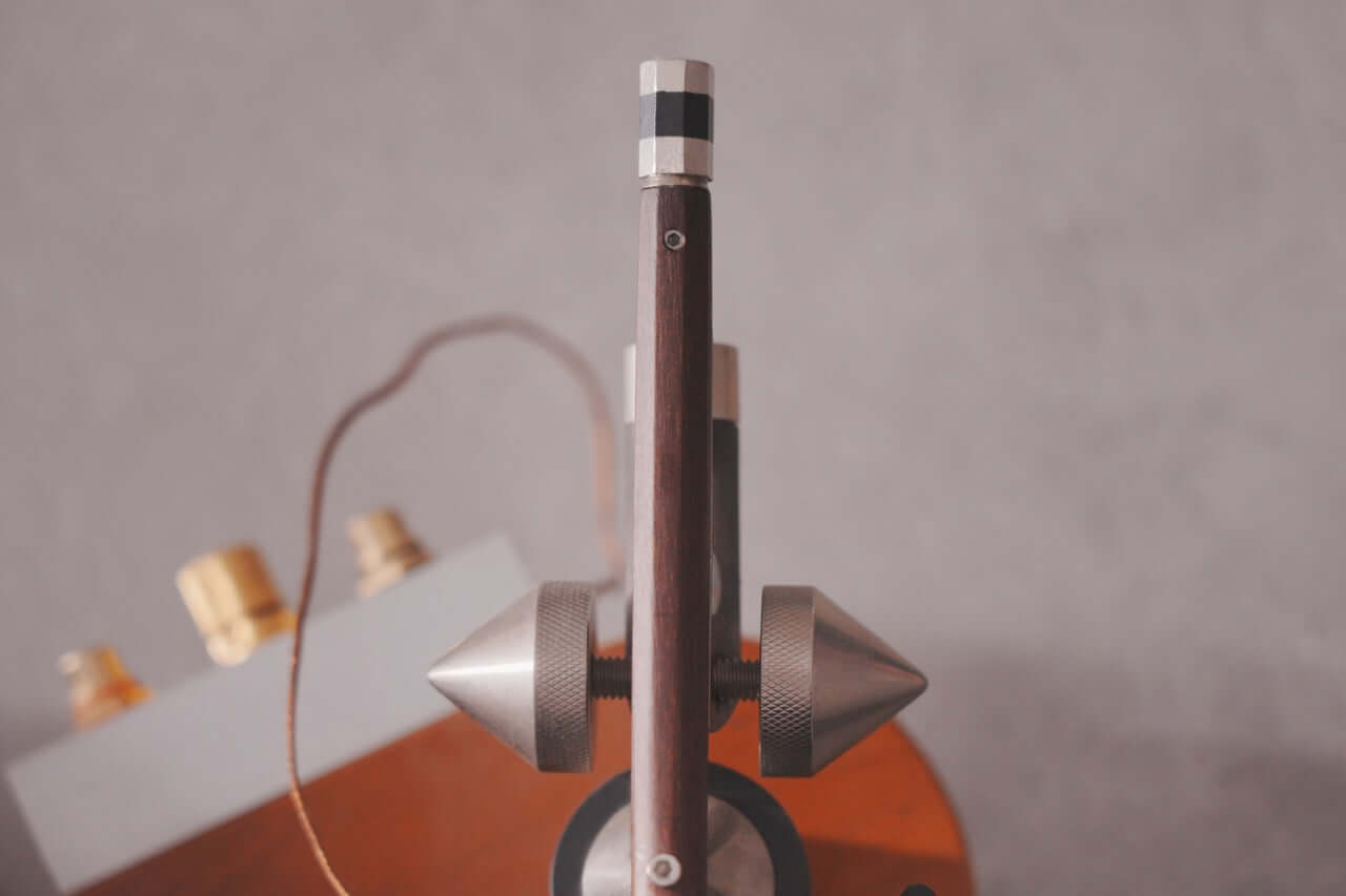 Close-up of fine tuners and strings on a violin or cello tailpiece, with blurred tuning pegs and body in the background, evoking the tactile elegance of the Arco 40 Plattenspieler wood turntable.
