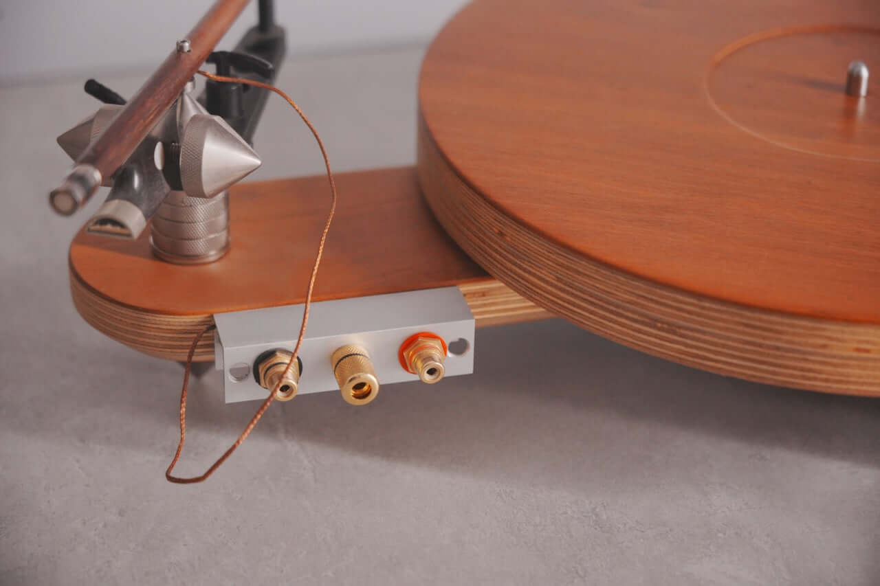 Close-up of the Arco 40 Plattenspieler wood turntable with visible tonearm and red and white RCA audio output connectors on a gray surface—ideal for vinyl enthusiasts.
