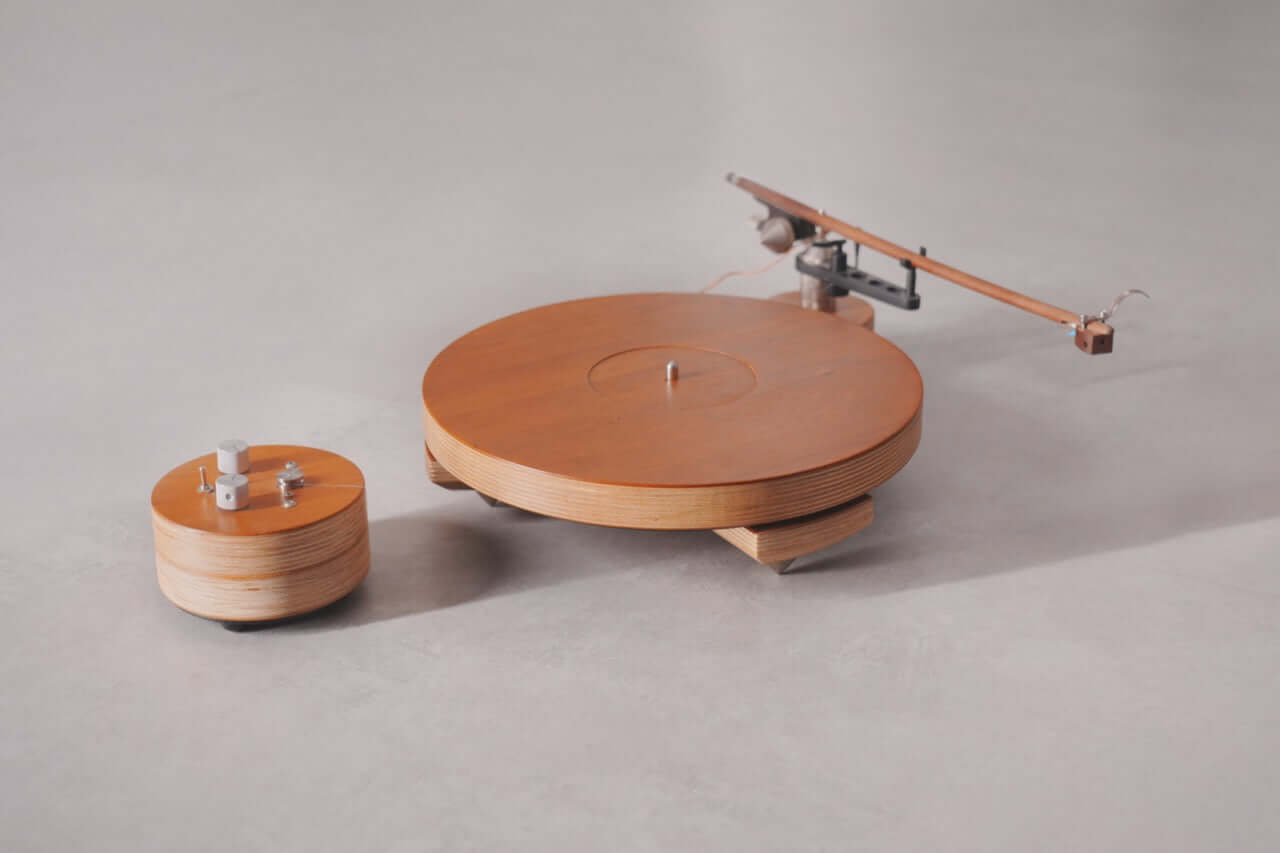 The Arco 40 Plattenspieler and its separate control unit, both with smooth, round designs and layered wood construction, rest on a light gray surface. Its long, slender tonearm is ideal for enjoying your favorite vinyl records.