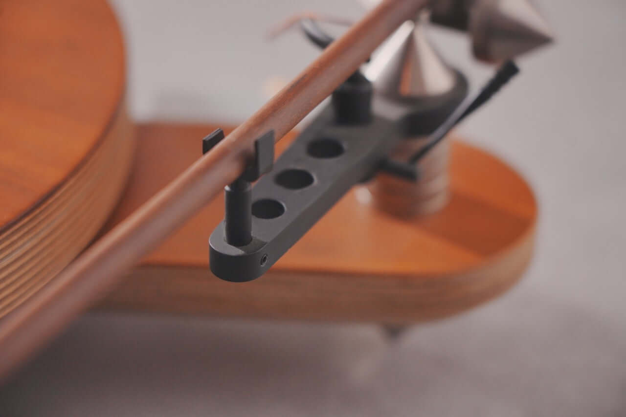 Close-up of the Arco 40 Plattenspieler’s tonearm and cartridge on a sleek wooden base with metal accents—ideal for vinyl lovers who value minimalist, modern design.
